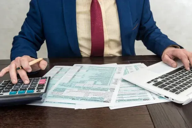 Person reviewing financial documents with a calculator and laptop