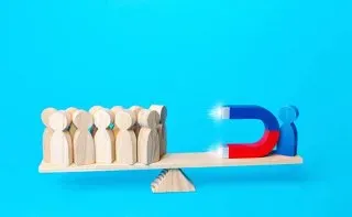 Magnet attracting wooden people on a balance, illustrating customer acquisition