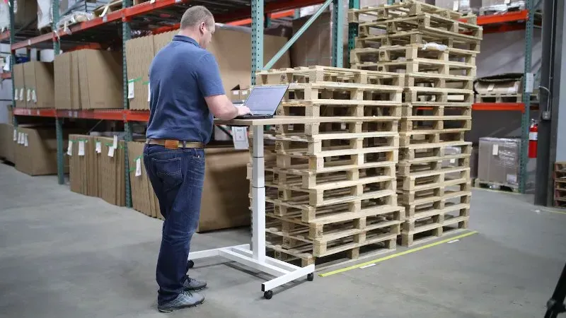 Warehouse worker using a computer beside stacked wooden pallets
