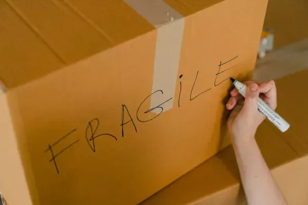 Person writing Fragile on a cardboard shipping box
