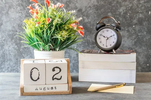 Desk calendar showing August 2 beside an alarm clock